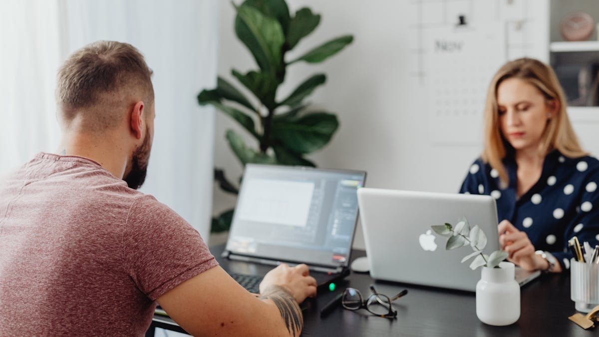 Two coworkers using laptops in a modern office setting, focusing on collaborative work.